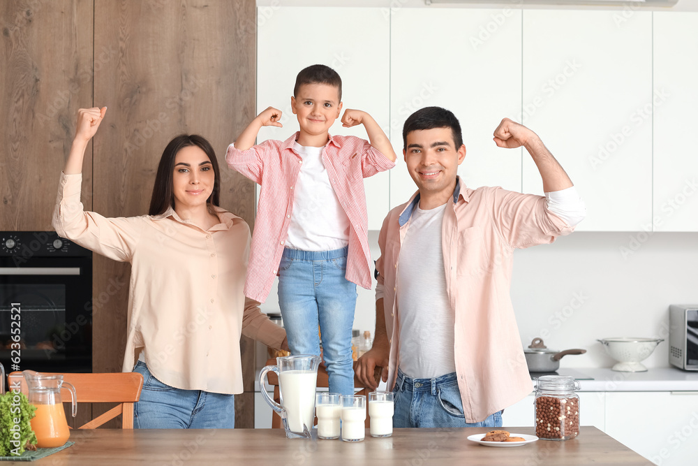 Happy family with milk showing muscles in kitchen