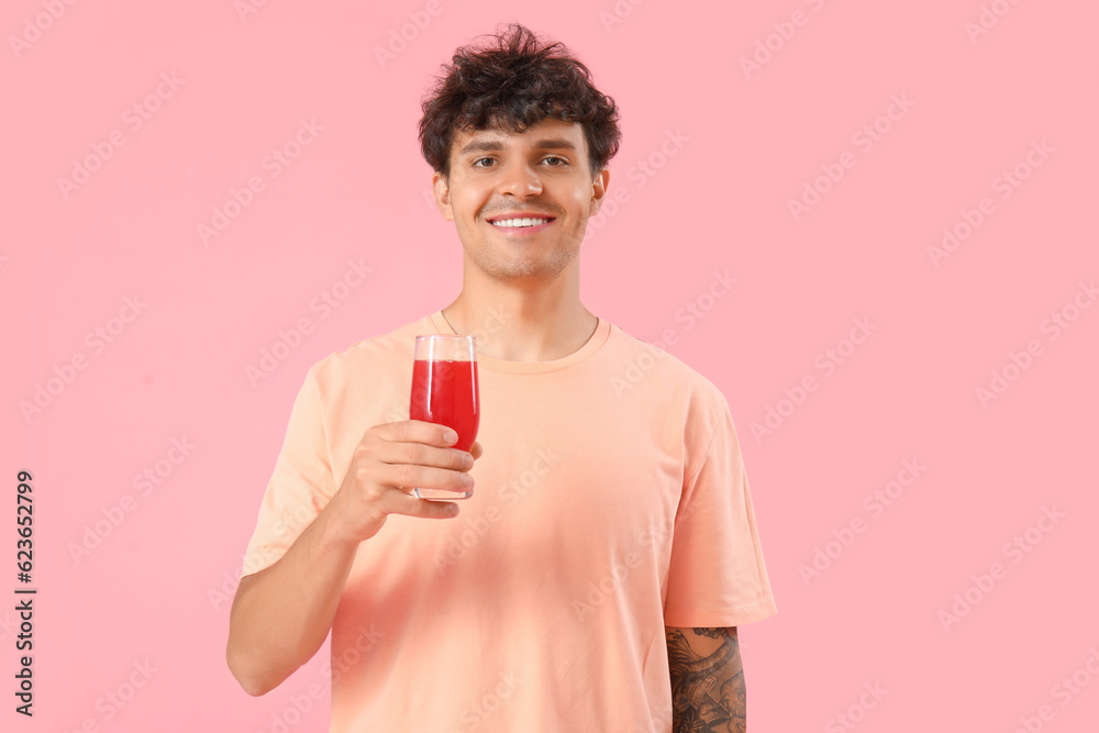 Young man with glass of red juice on pink background