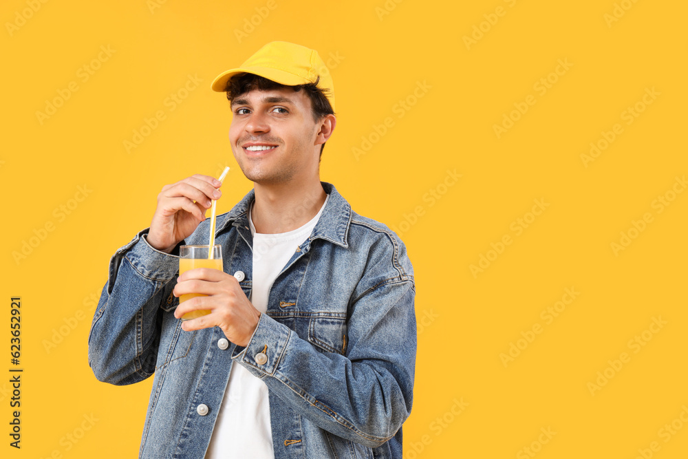 Young man with glass of orange juice on yellow background