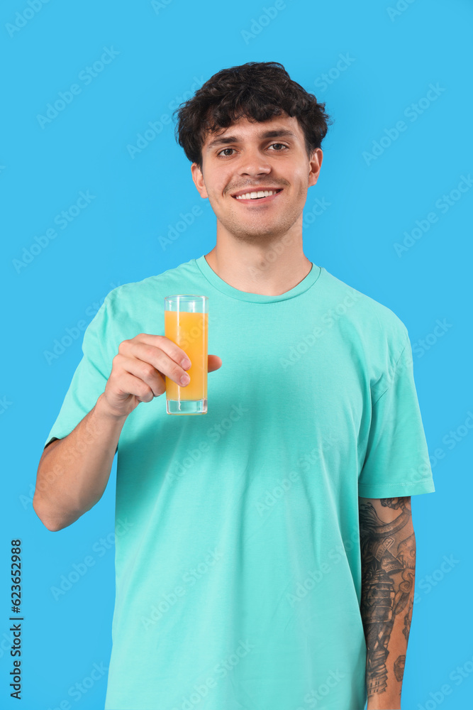 Young man with glass of orange juice on blue background