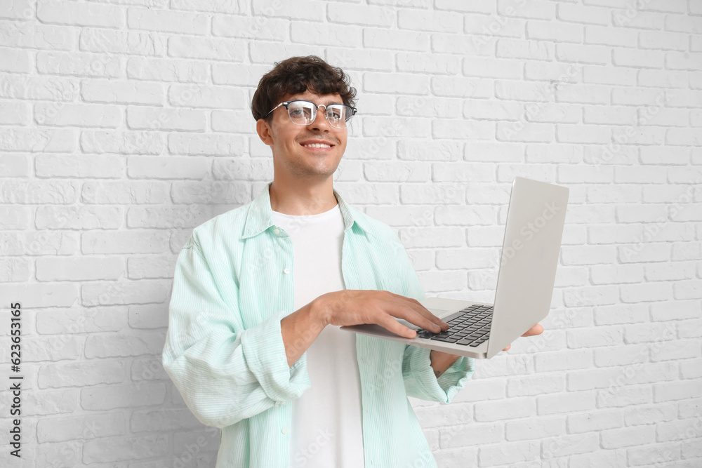 Male programmer working with laptop on white brick background