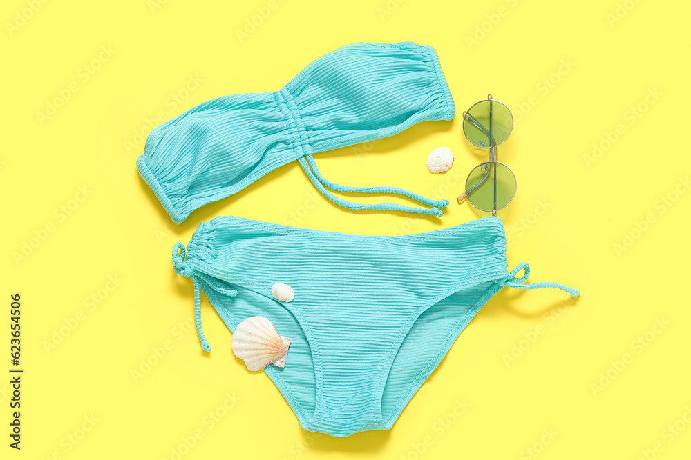 Stylish swimsuit, sunglasses and seashells on yellow background