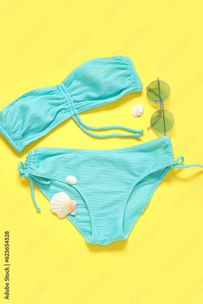 Stylish swimsuit, sunglasses and seashells on yellow background