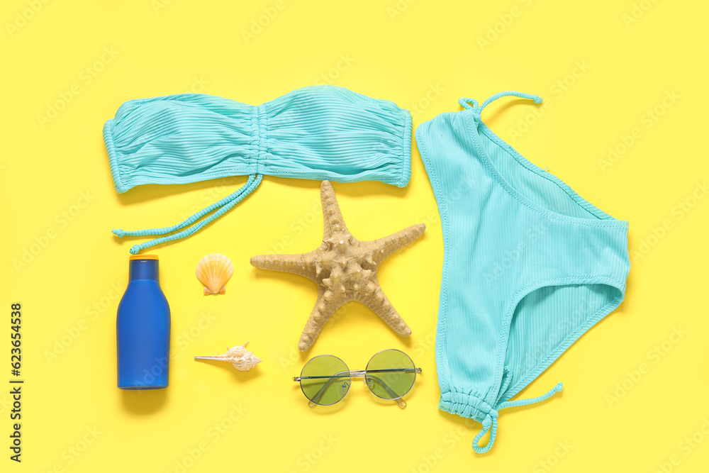 Composition with stylish swimsuit, sunglasses, bottle of sunscreen and seashells on yellow backgroun