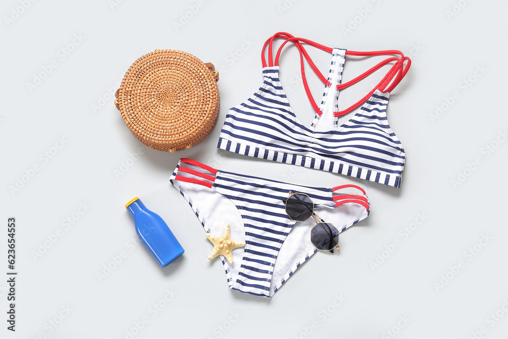 Stylish swimsuit, sunglasses, bag and bottle of sunscreen cream on light background