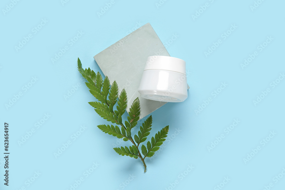 Plaster podium with jar of cosmetic product and fern leaf on color background