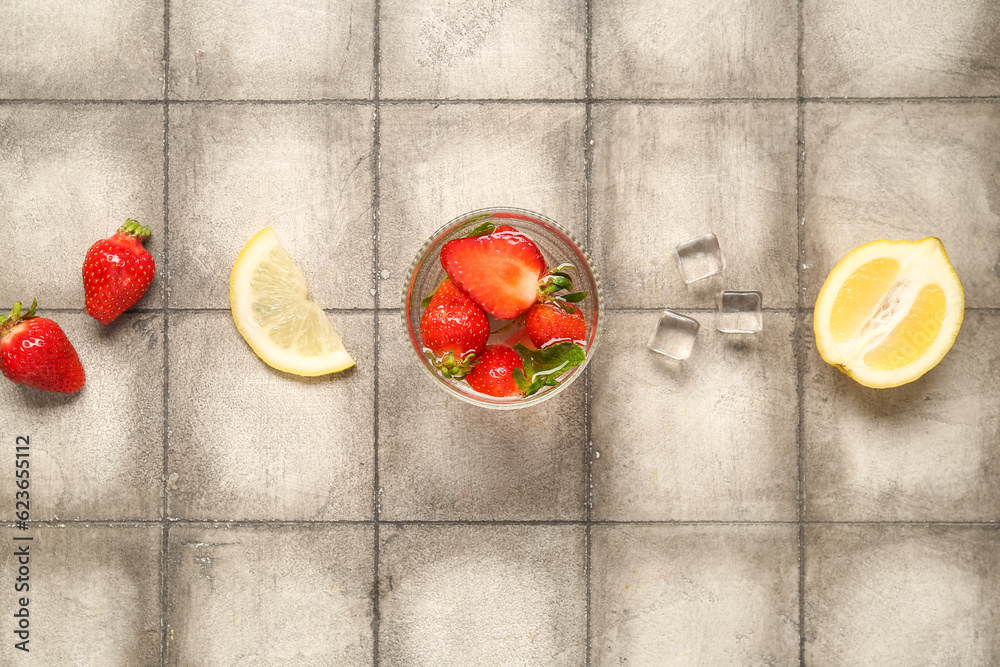 Glass of fresh lemonade with strawberry and lemon on grey tile background