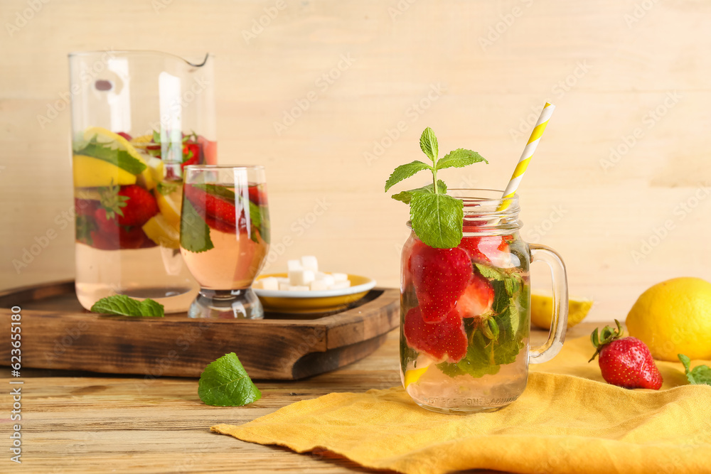 Mason jar and glass of fresh lemonade with strawberry on wooden table