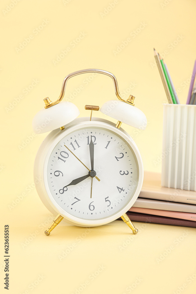 Alarm clock with notebooks and stationery holder on yellow background