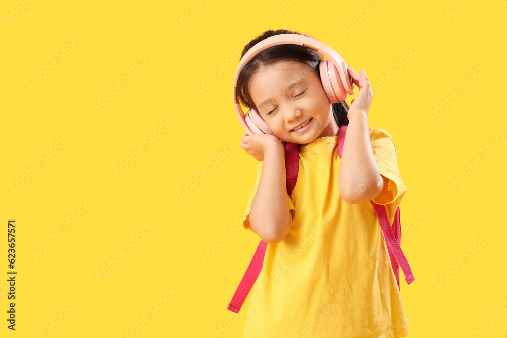 Little schoolgirl listening to music on yellow background