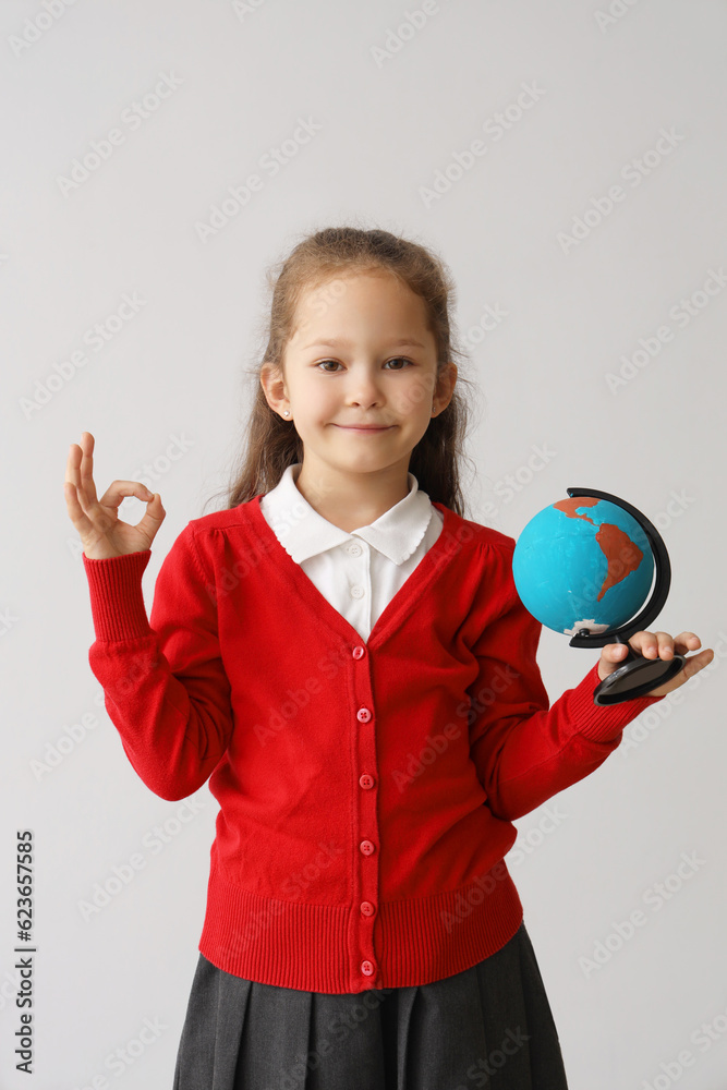 Little schoolgirl with globe showing OK on grey background