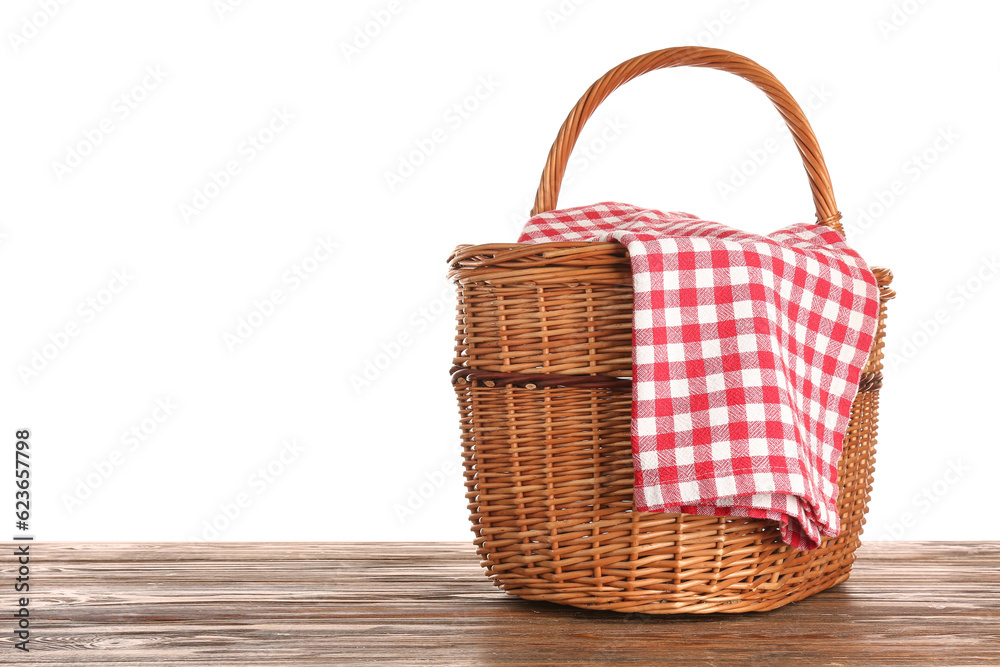 Wicker picnic basket with red checkered napkin on wooden table against white background