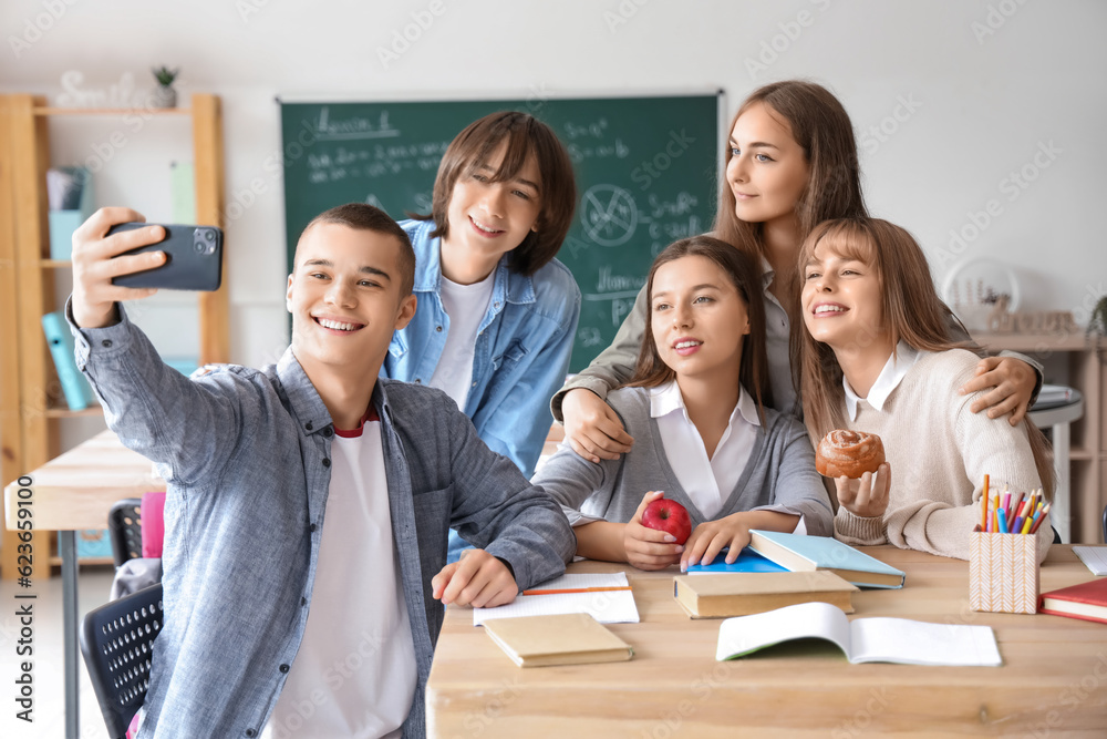 Group of teenage students taking selfie at table in classroom