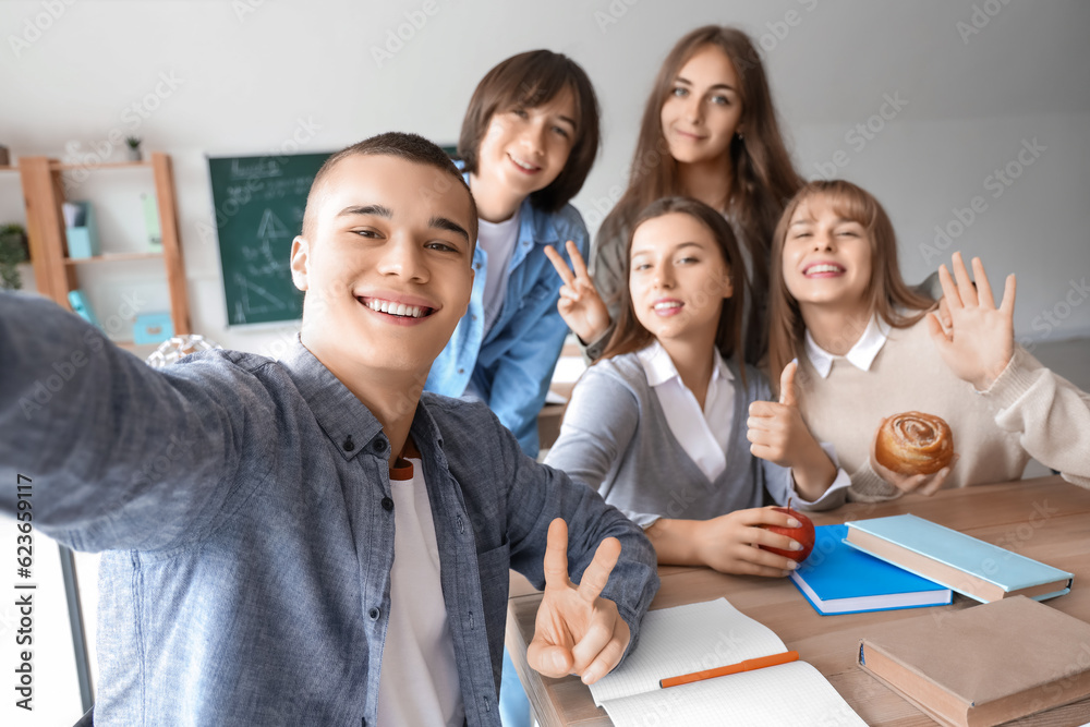 Group of teenage students taking selfie at table in classroom