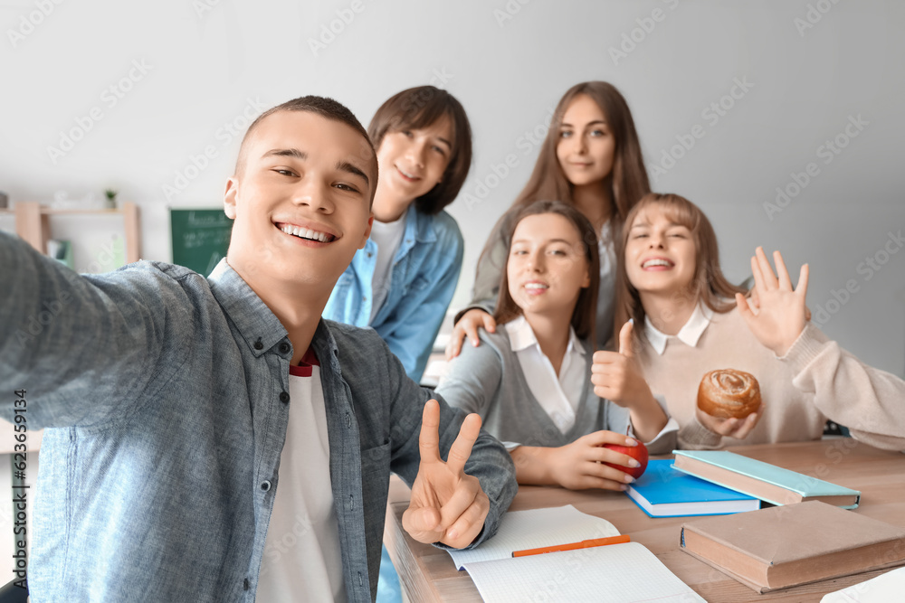 Group of teenage students taking selfie at table in classroom