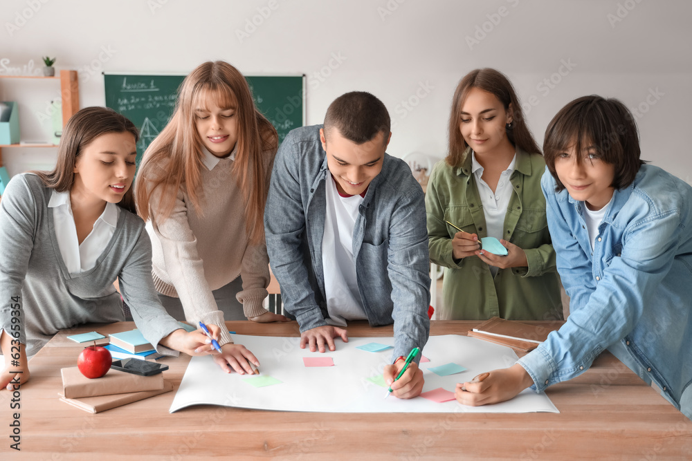 Group of teenage students performing task at table in classroom