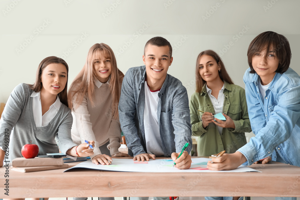 Group of teenage students performing task at table in classroom