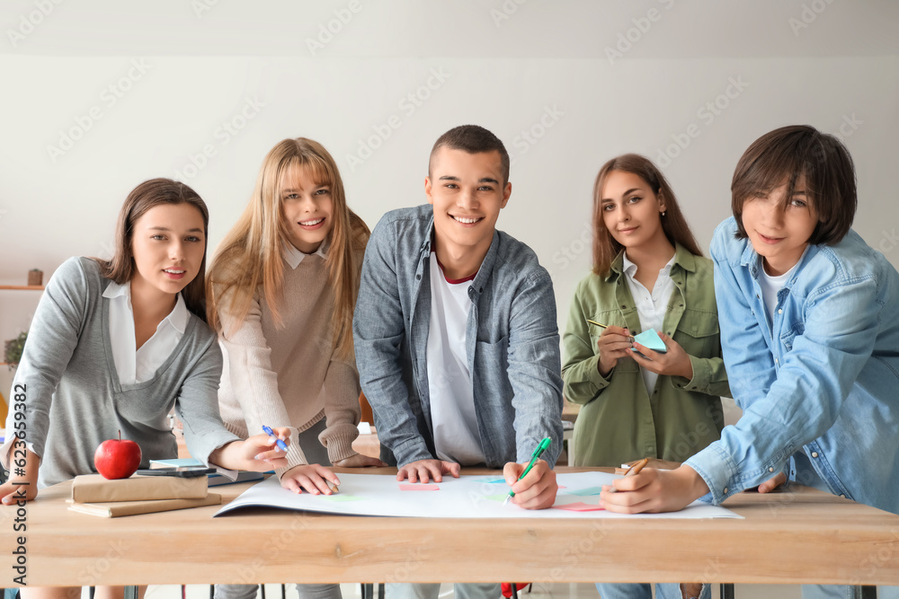 Group of teenage students performing task at table in classroom