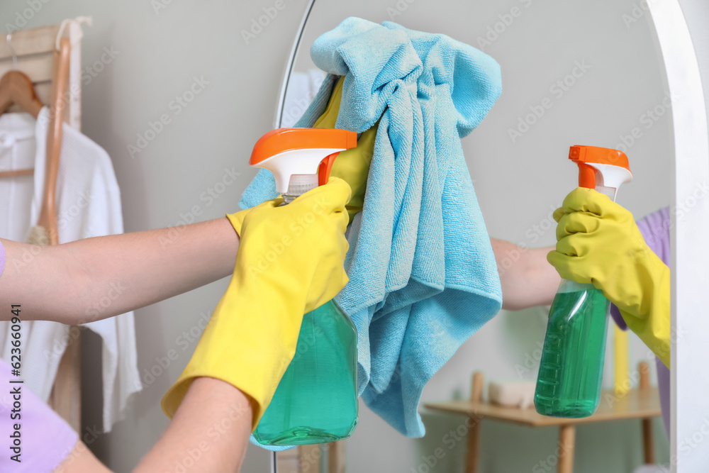 Young woman cleaning mirror in bathroom, closeup