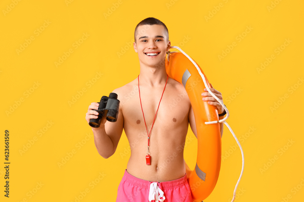 Male lifeguard with binoculars and ring buoy on yellow background