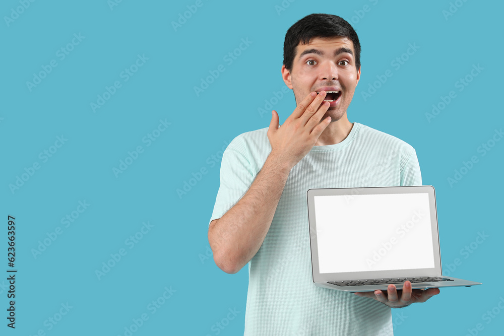 Surprised male programmer with laptop on blue background