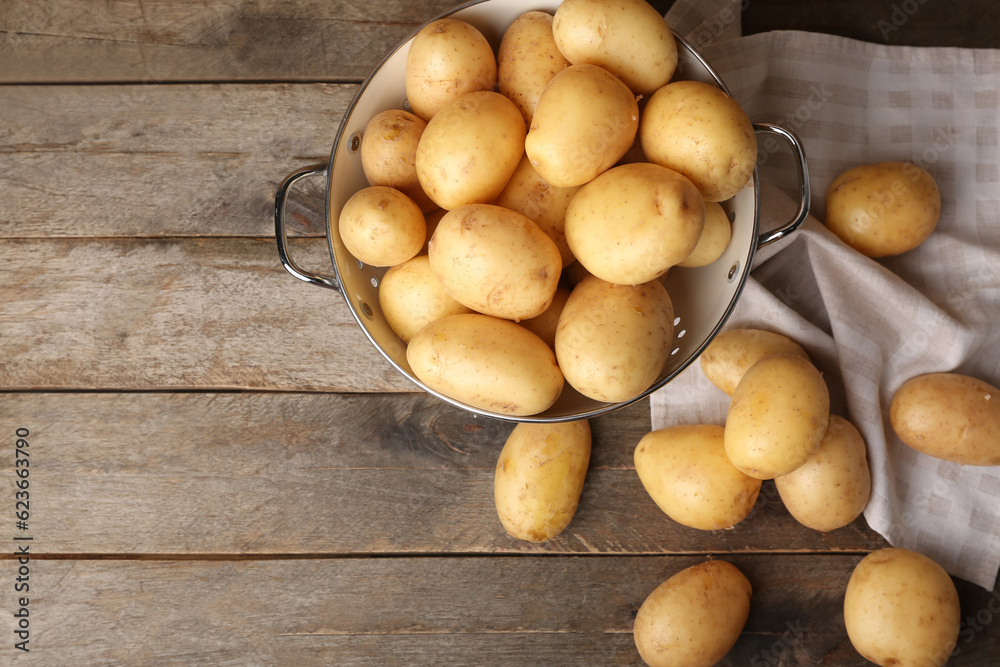 Colander with raw potatoes on wooden background