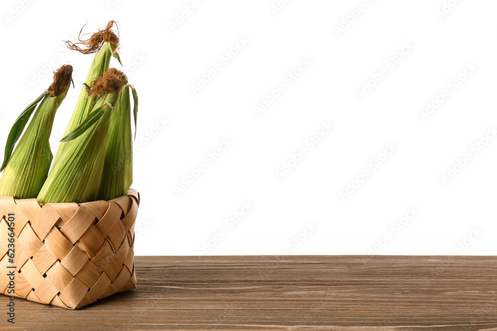 Wicker basket with fresh corn cobs on wooden table against white background