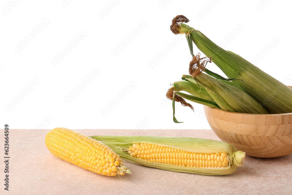 Bowl with fresh corn cobs on pink table against white background