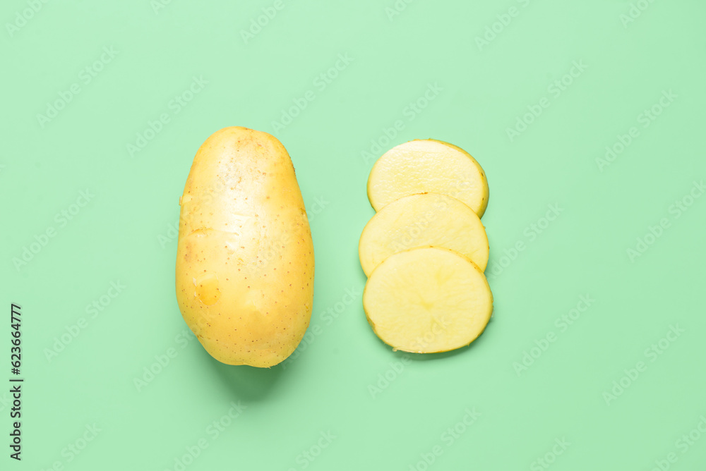 Whole and cut potatoes on green background