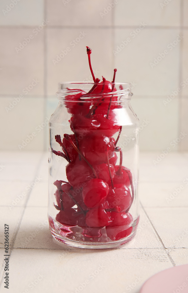 Jar with tasty maraschino cherries on white tile background