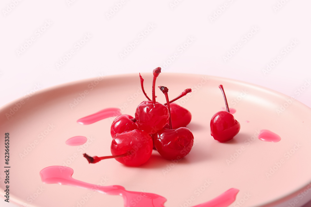 Plate with tasty maraschino cherries on pink background