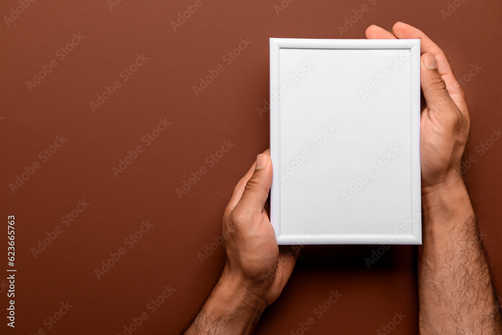 Man holding blank photo frame on brown background