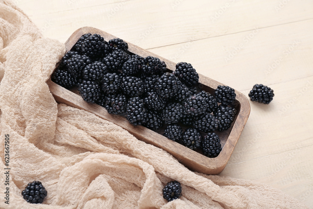 Board with fresh blackberry on light wooden background, closeup