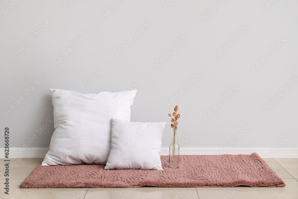 Pillows and vase with dried flowers on carpet near white wall