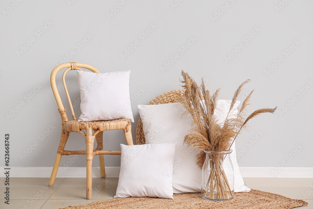 Wicker chair, pillows and vase with pampas grass near white wall