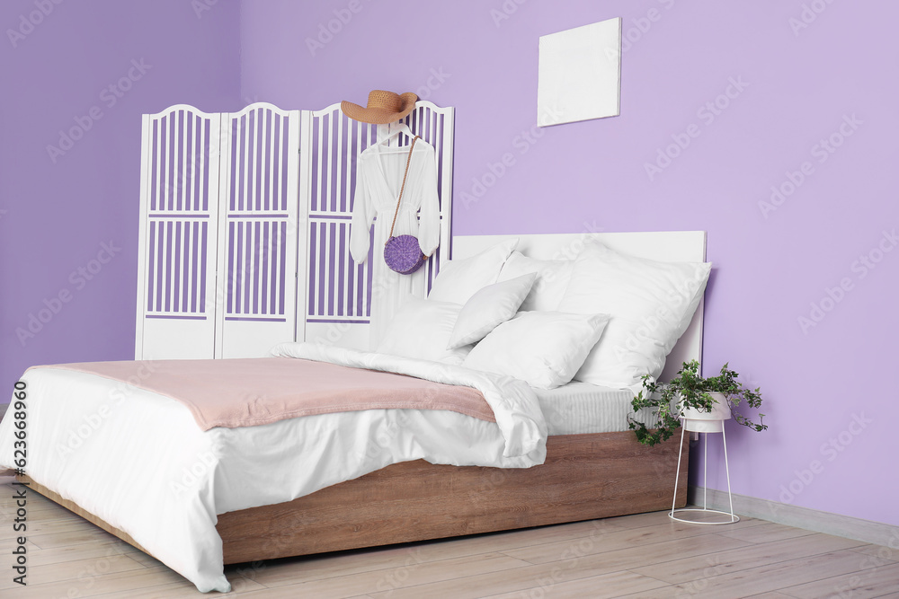 Interior of stylish bedroom with comfortable bed, white pillows and dress on folding screen