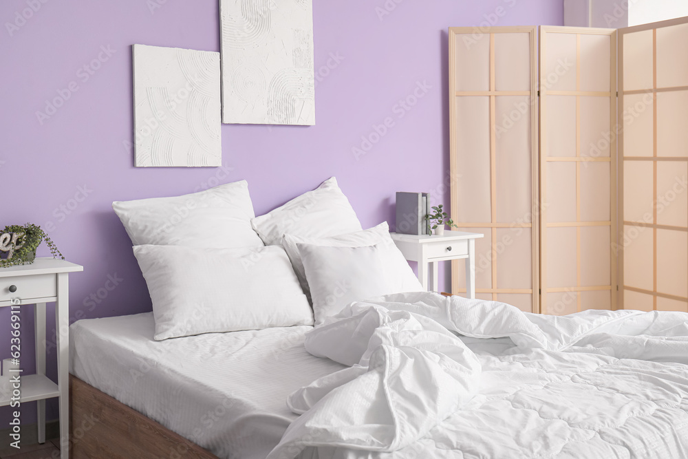 Interior of stylish bedroom with comfortable bed, white pillows, bedside tables and folding screen