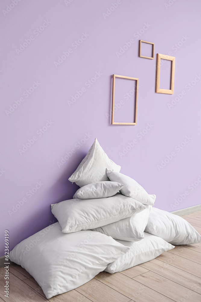 Pile of white pillows blank frames near lilac wall