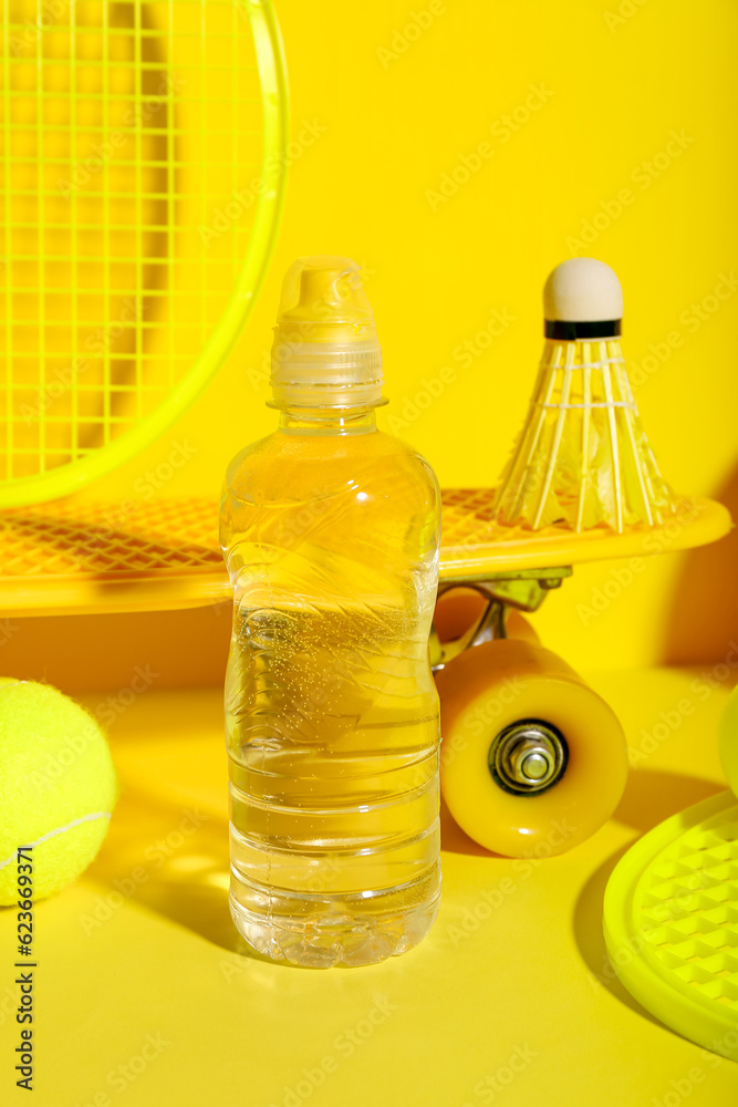 Set of sports equipment with bottle of water on yellow background