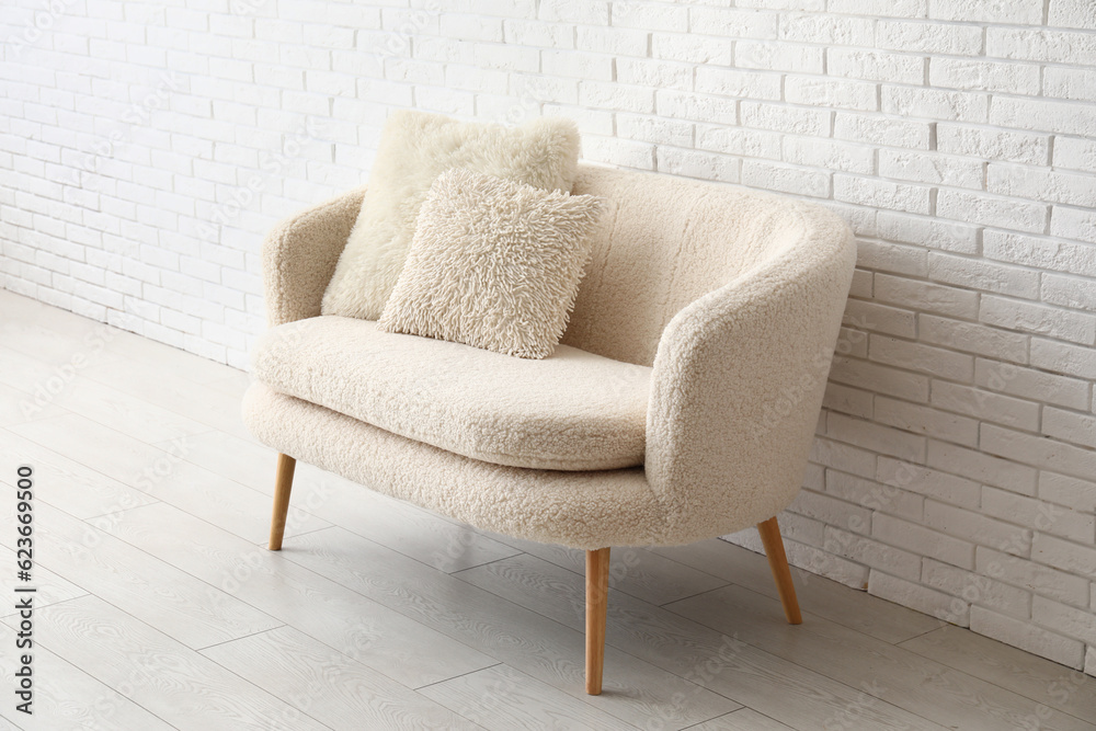 Cozy white sofa with pillows near brick wall