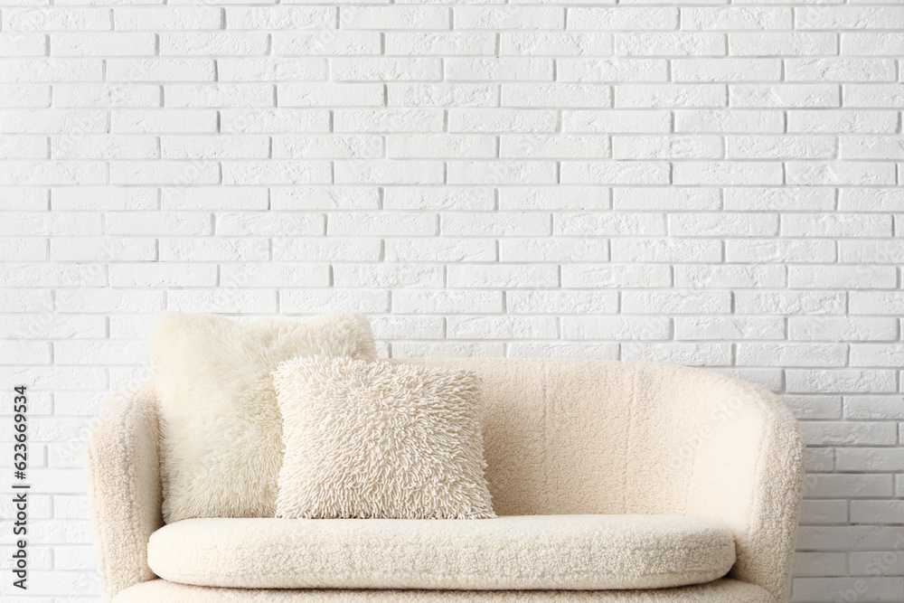 Cozy white sofa with pillows near brick wall