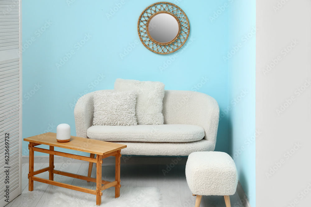 Cozy white sofa, table and ottoman near blue wall