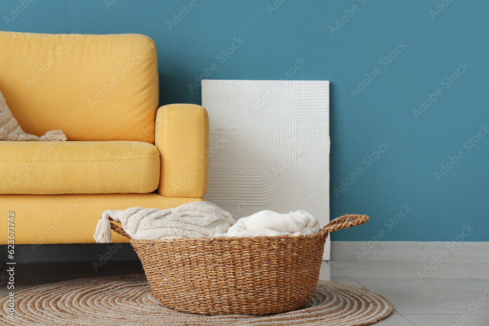 Yellow armchair and wicker basket with cushions near blue wall