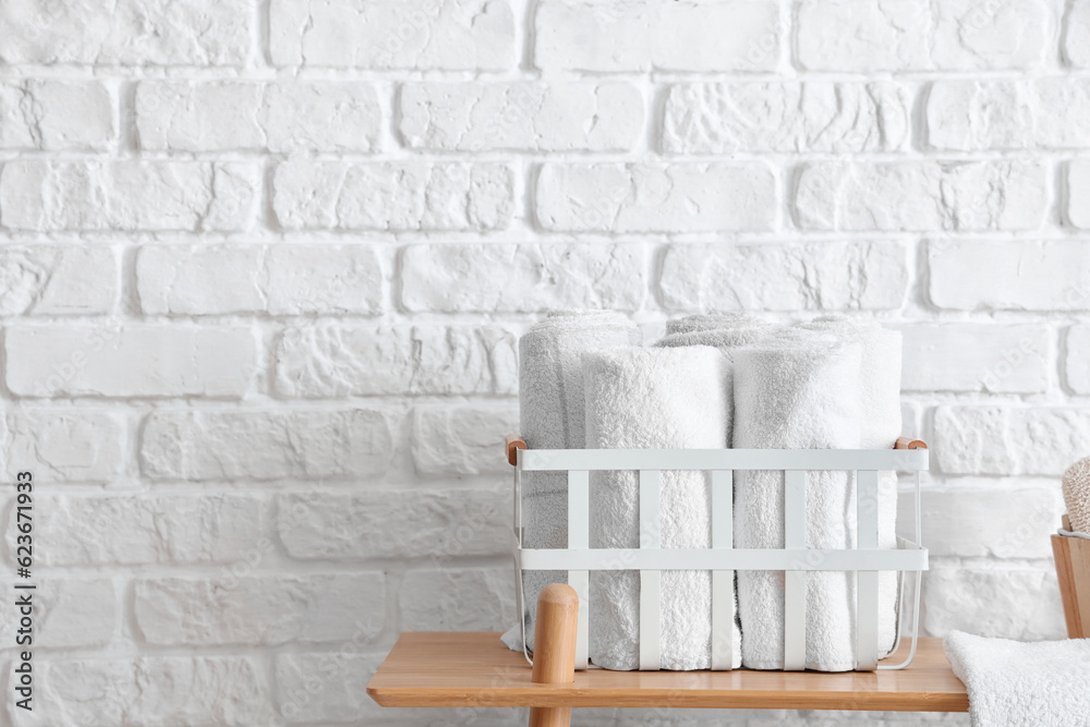 Basket with rolled towels on wooden shelving unit near white brick wall