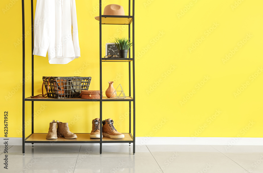 Shelving unit with white shirt, purses in basket, shoes and hat near yellow wall