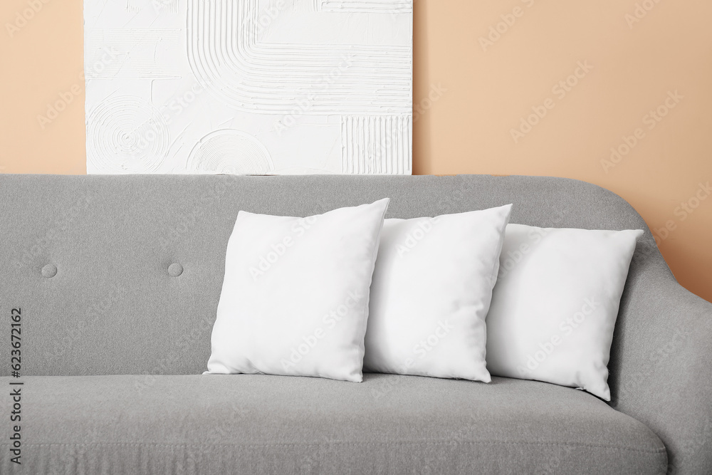 Grey sofa with white pillows near beige wall