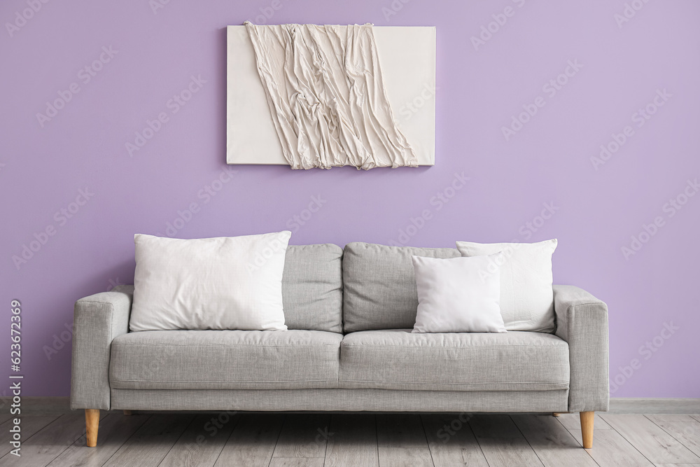 Grey sofa with white pillows near lilac wall