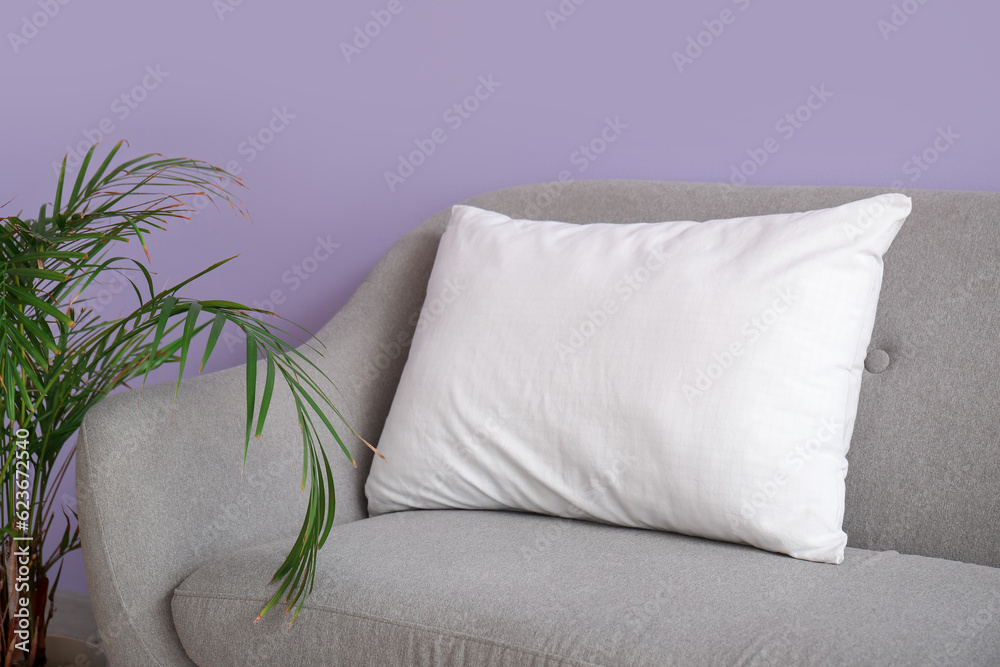 Grey sofa with white pillow near lilac wall