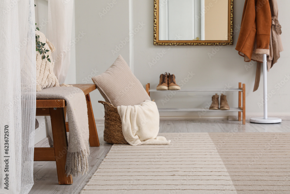 Wooden bench, wicker basket with cushion and shoes stand in interior of hallway