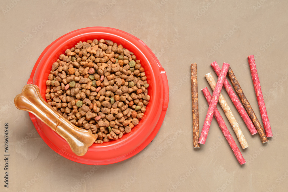 Bowl with dry dog food and treats on color background